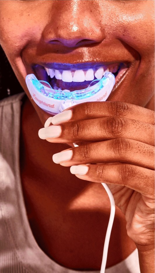 The Laughland whitening mouthpiece held in front of the mouth, its arch glowing blue from the light inside