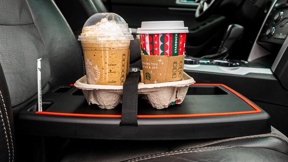 The Stupid Car Tray set up inside a car holding a cup and a laptop